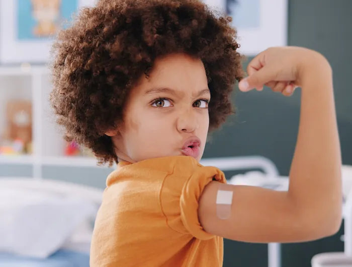 young child flexing muscles showing off a band-aid on their vaccine sight