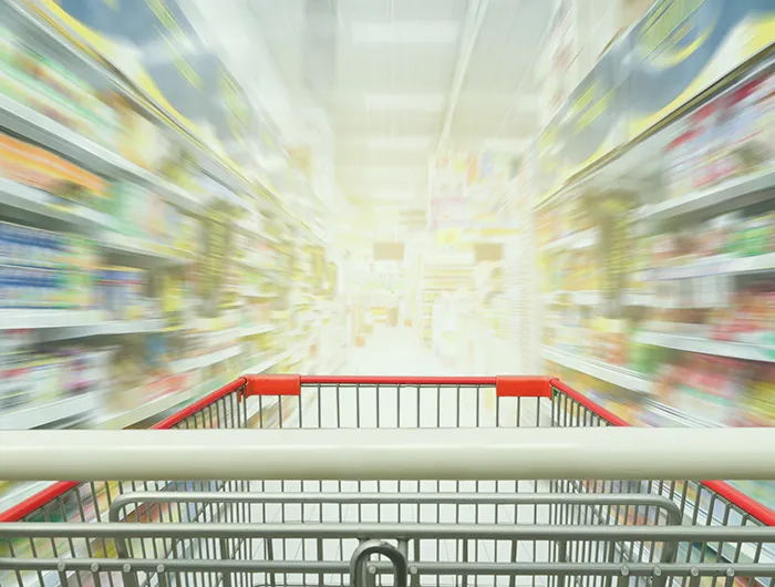 grocery cart in focus in the foreground with grocery store shelves out of focus in the background