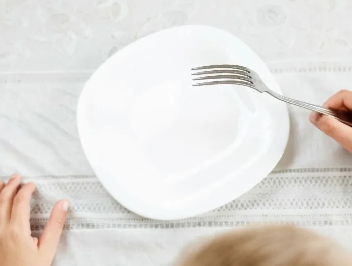 A child holds a fork over an empty plate
