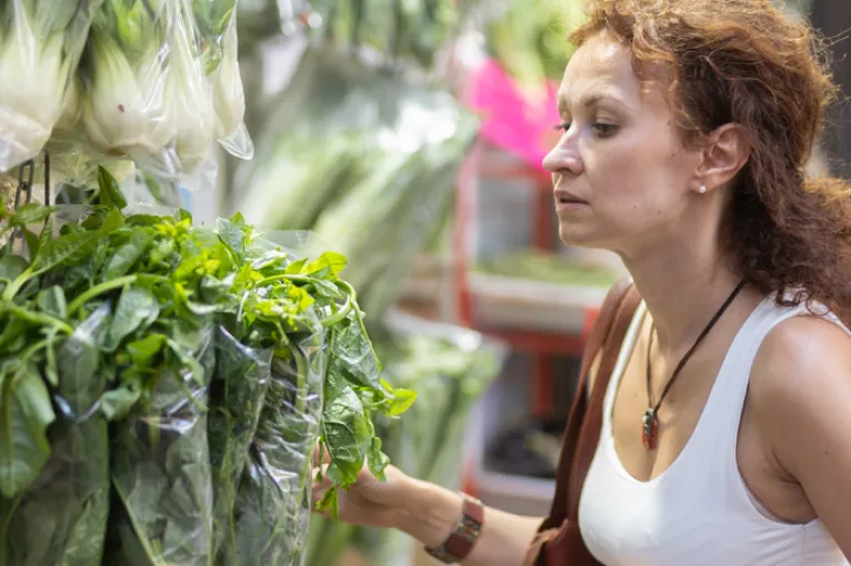 woman choosing a bunch of leafy greens in grocery store