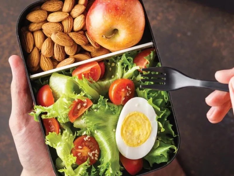 box of food with a salad, egg, almonds, and apple