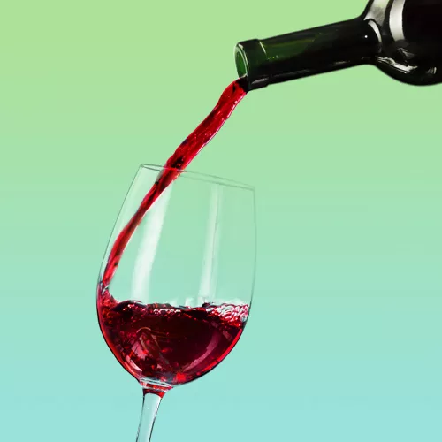 bottle of red wine pouring into clear wine glass