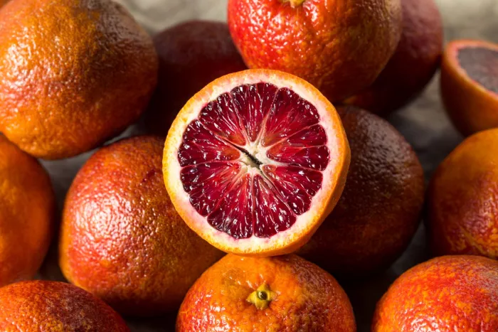 seasonal produce - a bowl of whole blood oranges from above, with a single blood orange cut in half