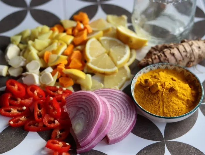 Fire cider chopped ingredients on grey tiled background. Top view photo of turmeric, ginger, pepper, garlic, onion and lemon.