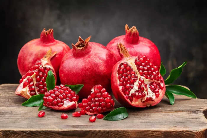 Seasonal produce - Several ripe pomegranate fruits and an open pomegranate with pomegranate leaves on a wooden old cutting board, side view, dark background