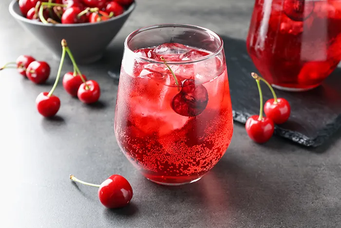 clear glass with ice and sparkling red juice surrounded by cherries