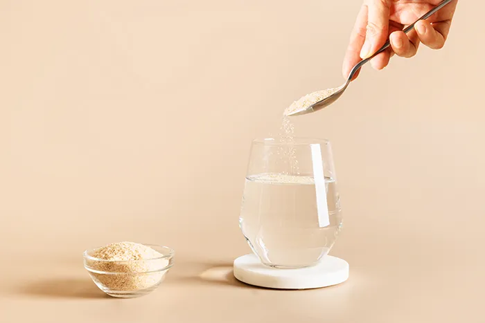 spoon pouring psyllium powder into clear glass of water