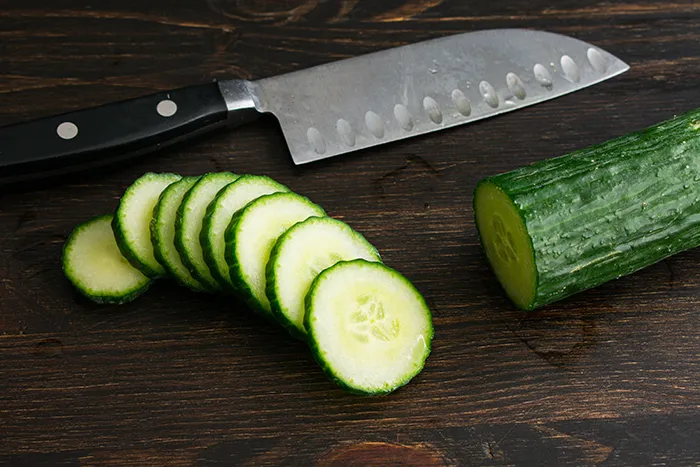 knife with half sliced and half whole cucumber on cutting board
