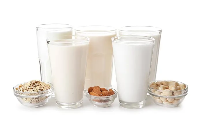 5 glasses of different kinds of milk with 3 bowls of oats, almonds, and soy beans