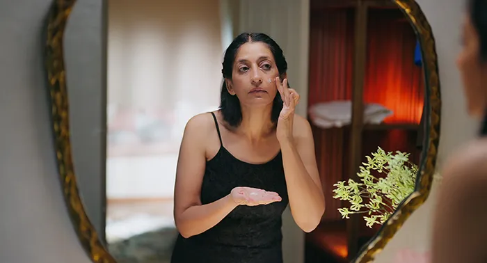 woman looking in mirror and rubbing topical cream onto her cheek