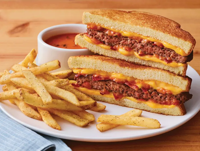 cheeseburger grilled cheese on a plate with fries and small bowl of tomato soup.