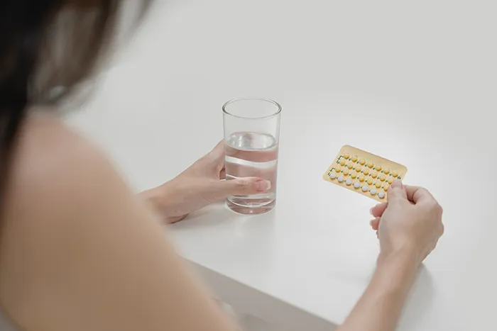 woman holding birth control pill pack and glass of water