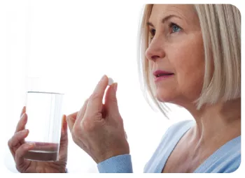 woman holding a glass of water and supplement close to her mouth
