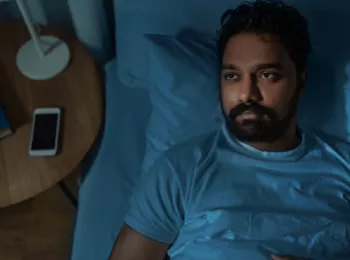 man lying in bed staring up at the ceiling at night