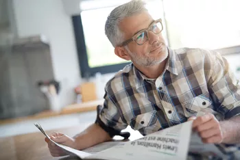 older man waring glasses and holding a newspaper 