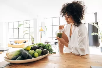 woman drinking green smoothie with green fruit in the foreground