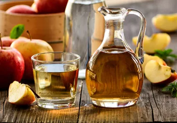 clear jug of vinegar with clear cup of vinegar with apples in the same background.