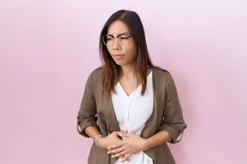woman holding her stomach in pain in front of a pink background