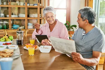 older couple sitting at dining table while eating and reading
