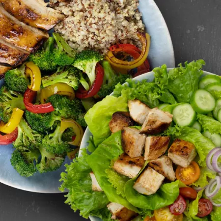 plate of chicken, vegetables, and quinoa alongside plate of chicken salad