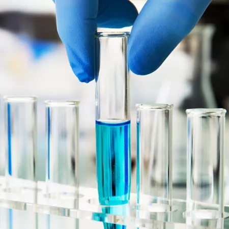 row test tubes one being held by a hand with gloves contains blue liquid