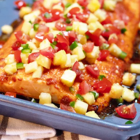 large piece of salmon covered in pineapple and tomato salsa on a pan