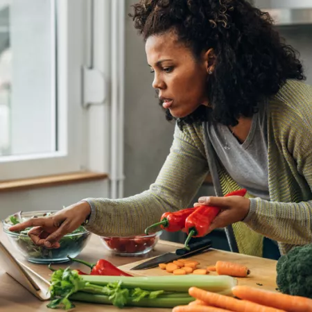 woman checking ipad while cutting vegetables in kitchen