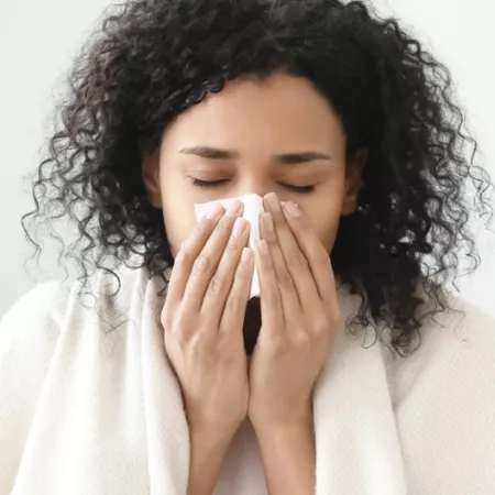 woman with blanket around her shoulders blowing her nose