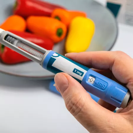 hand holding an obesity medication applicator with bell peppers in the background