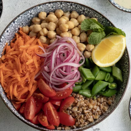 bowl filled with un-mixed vegetables like shredded carrots, red onion, chickpeas, and more