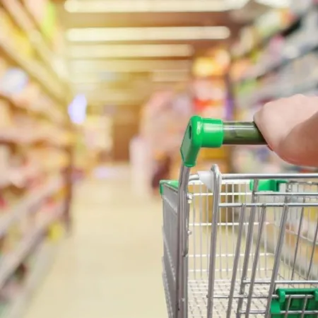 A grocery cart with a green handle in a grocery store aisle