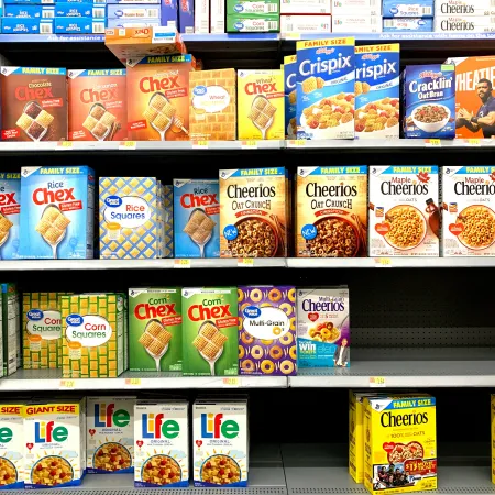 A cereal aisle displaying Cheerios variations, Chex, Wheaties, Life Cereal, and more.