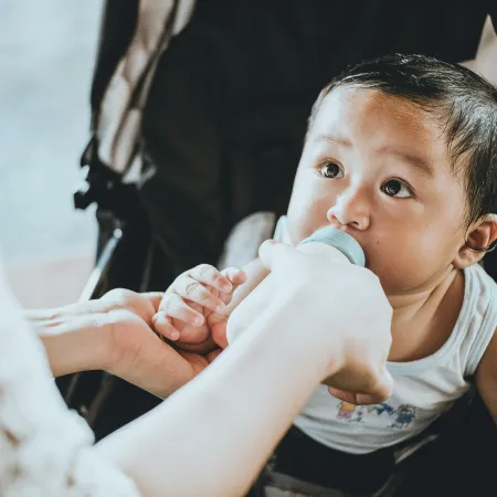 A baby in a stroller being fed from a bottle.