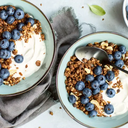 two blue bowls filled with yogurt, granola and blueberries